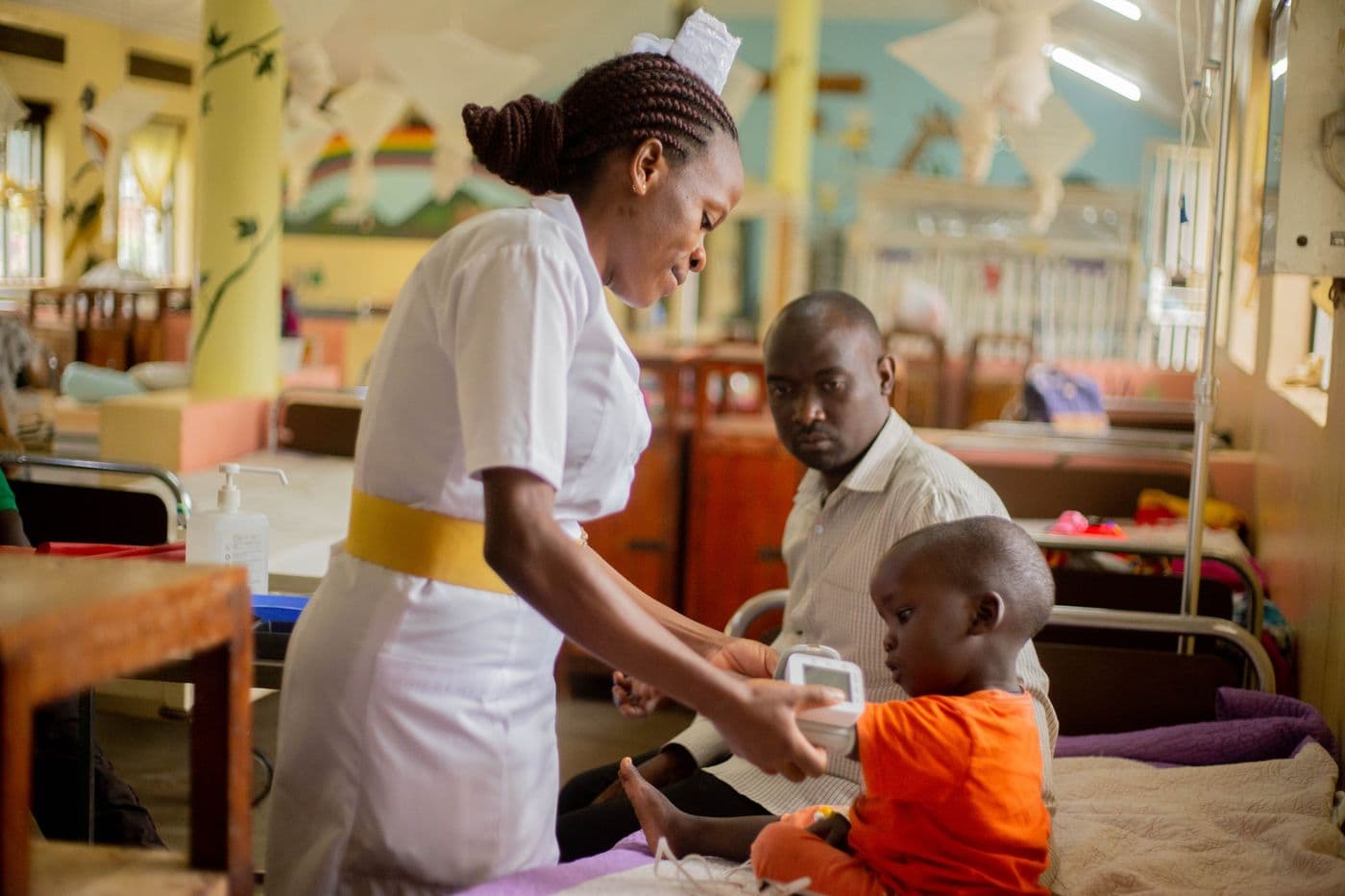 Nurse providing attentive care to a young patient in a hospital ward while a family member watches